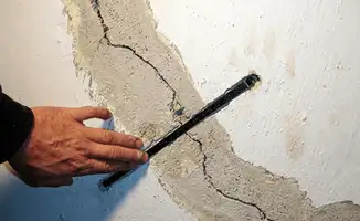 A wall with a large crack is being inspected by a professional in Anchorage, AK